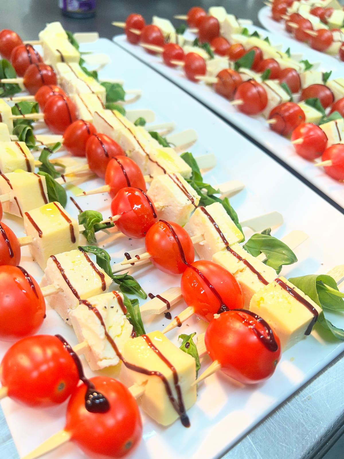 Trays of caprese skewers with cherry tomato, cheese, basil and balsamic glaze prepared for a private function